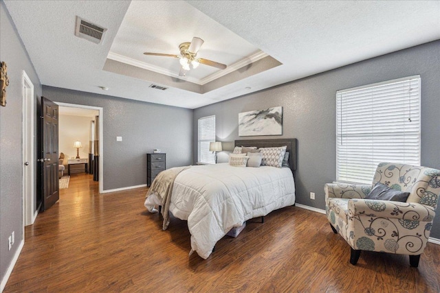 bedroom featuring visible vents, wood finished floors, a raised ceiling, and ornamental molding