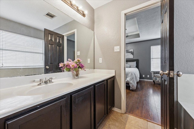 ensuite bathroom featuring tile patterned floors, vanity, visible vents, and a textured wall