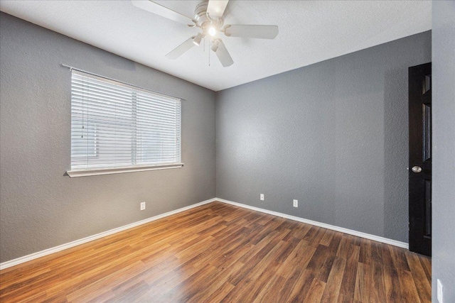 empty room featuring a textured wall, baseboards, a ceiling fan, and wood finished floors