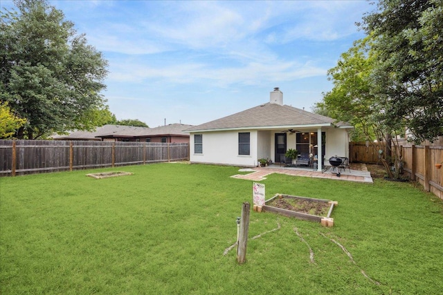rear view of house featuring a patio, a ceiling fan, a chimney, a lawn, and a fenced backyard