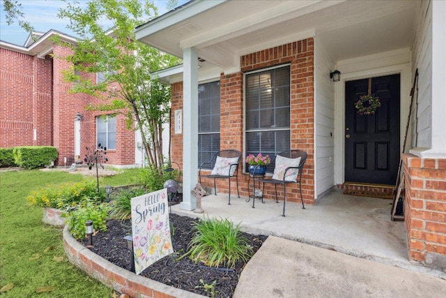 view of exterior entry featuring covered porch and brick siding