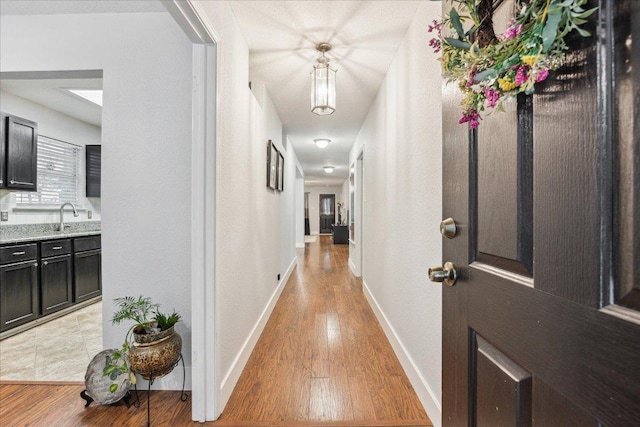 hall with a sink, baseboards, and light wood-style floors