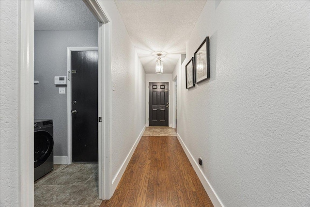 corridor with a textured ceiling, a textured wall, and washer / dryer