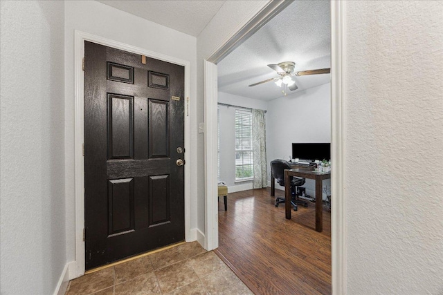 foyer featuring baseboards, ceiling fan, and a textured wall
