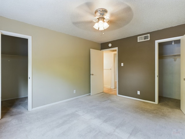 unfurnished bedroom with a closet, a textured ceiling, visible vents, a walk in closet, and light colored carpet