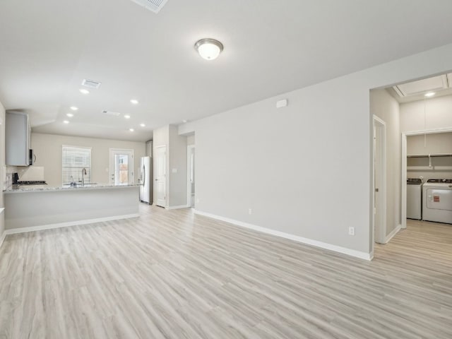 unfurnished living room featuring baseboards, light wood finished floors, and washer and clothes dryer