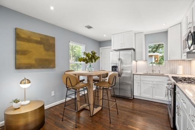 kitchen featuring stainless steel appliances, white cabinetry, baseboards, decorative backsplash, and dark wood-style floors