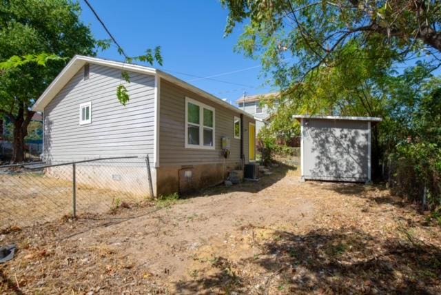 view of home's exterior featuring fence, a storage shed, an outbuilding, and central AC