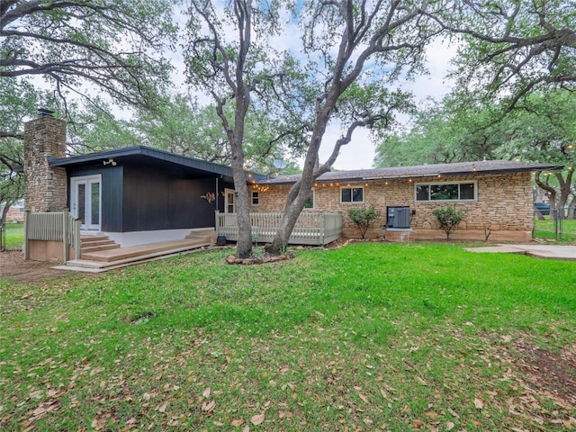 rear view of property with stone siding, a lawn, a wooden deck, a chimney, and central AC unit