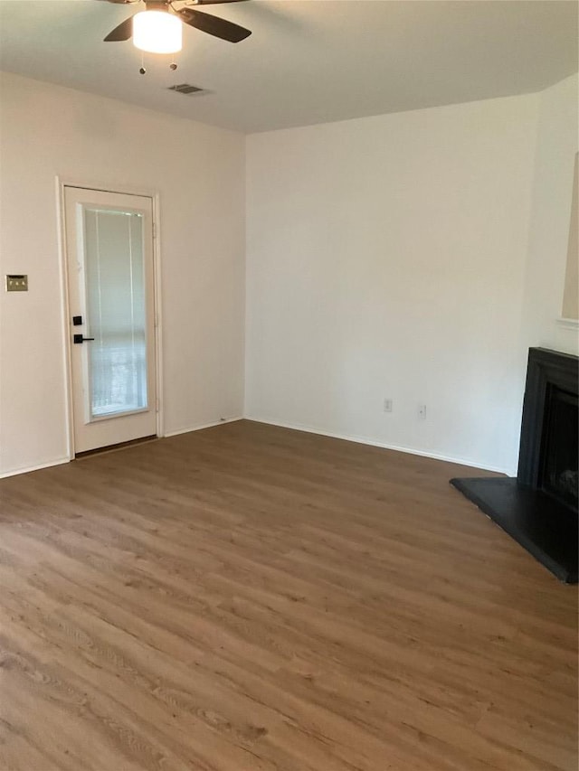 unfurnished living room with visible vents, wood finished floors, a fireplace with raised hearth, and ceiling fan