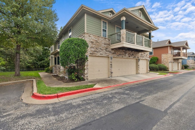 view of front of property with driveway, a garage, stone siding, and a balcony