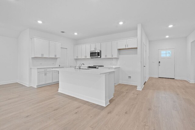 409 Rivers Edge Dr, Georgetown, TX 78628 - kitchen with an island with sink, white cabinets, stainless steel microwave, light countertops, and tasteful backsplash
