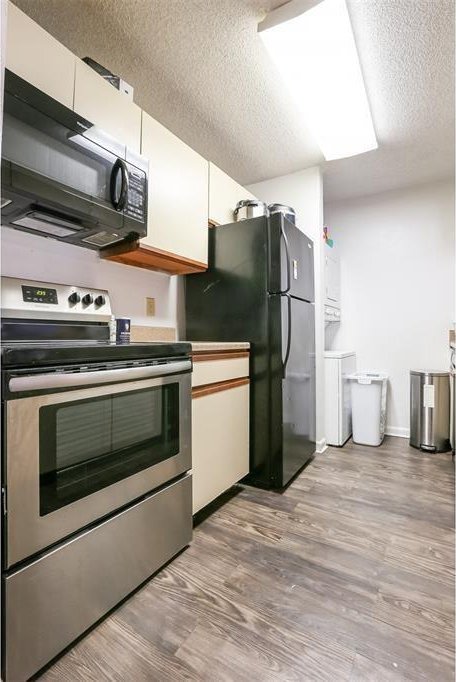 912 W 22nd St Unit 307, Austin, TX 78705 - kitchen with black appliances, a textured ceiling, wood finished floors, and white cabinetry