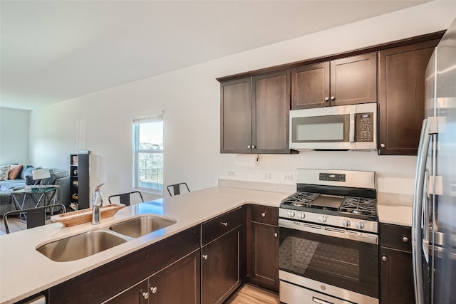 kitchen with dark brown cabinets, a sink, open floor plan, light countertops, and appliances with stainless steel finishes