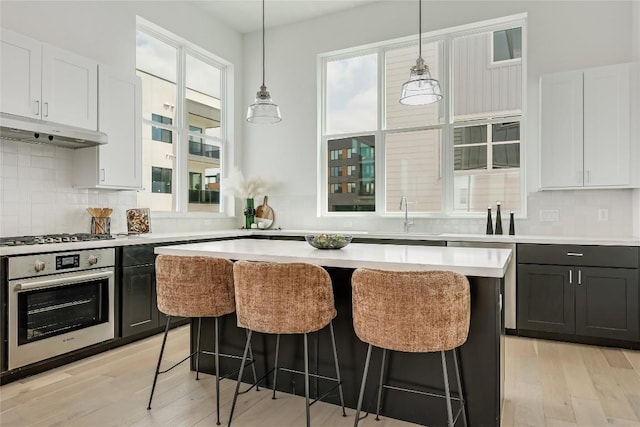 kitchen featuring stainless steel appliances, a kitchen bar, under cabinet range hood, and plenty of natural light