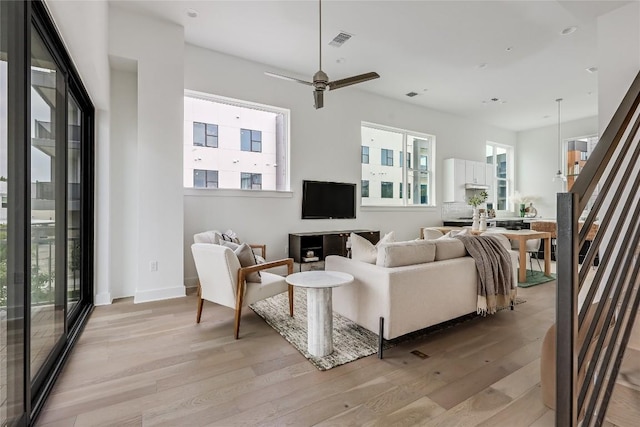 living room featuring baseboards, a ceiling fan, visible vents, and light wood-style floors