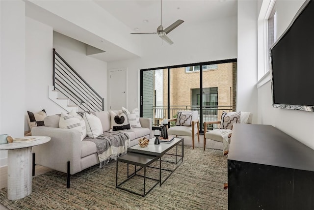 living area with stairway, a high ceiling, a ceiling fan, and wood finished floors