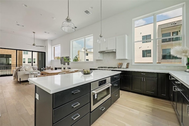 kitchen with stainless steel oven, dark cabinets, visible vents, and light wood-style flooring