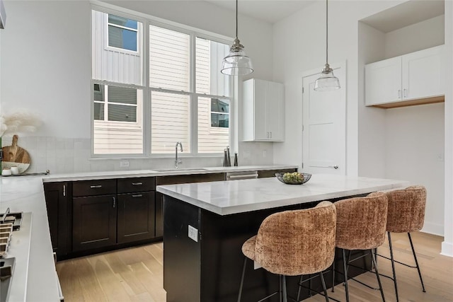 kitchen featuring hanging light fixtures, a kitchen bar, a sink, white cabinetry, and light wood-style floors