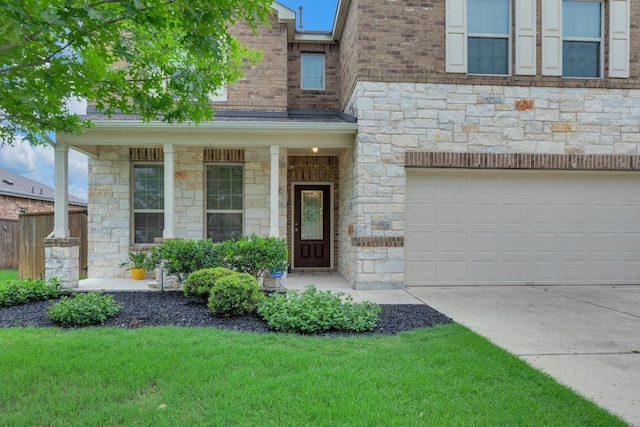 entrance to property with concrete driveway, stone siding, a yard, and covered porch