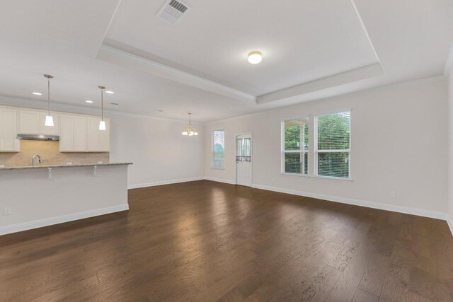 unfurnished living room featuring ornamental molding, an inviting chandelier, a tray ceiling, and visible vents