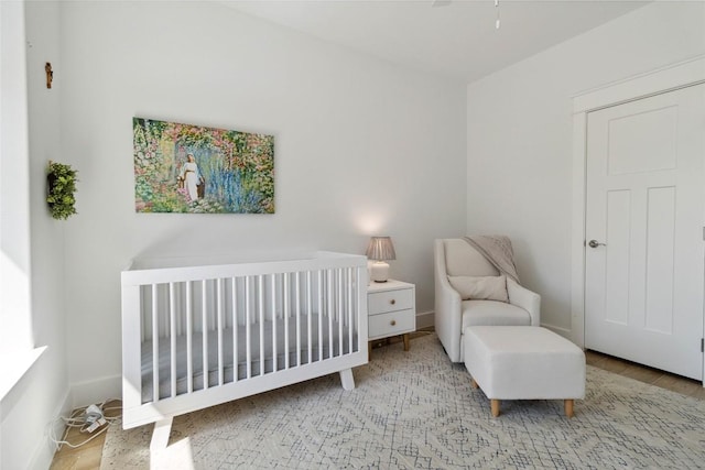 bedroom featuring baseboards, a crib, and wood finished floors