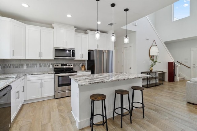 kitchen with light wood-style flooring, a breakfast bar, white cabinets, backsplash, and appliances with stainless steel finishes