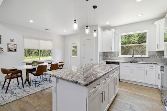 kitchen with light stone counters, a sink, white cabinetry, decorative backsplash, and a kitchen island
