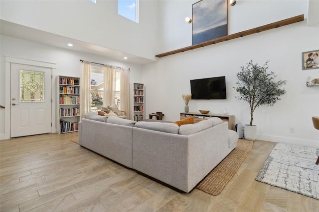 living room with baseboards, light wood-style flooring, recessed lighting, and a high ceiling
