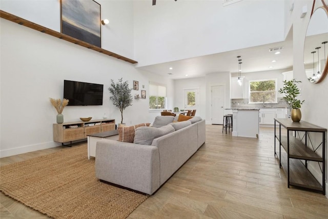 living room featuring light wood finished floors, a high ceiling, visible vents, and recessed lighting