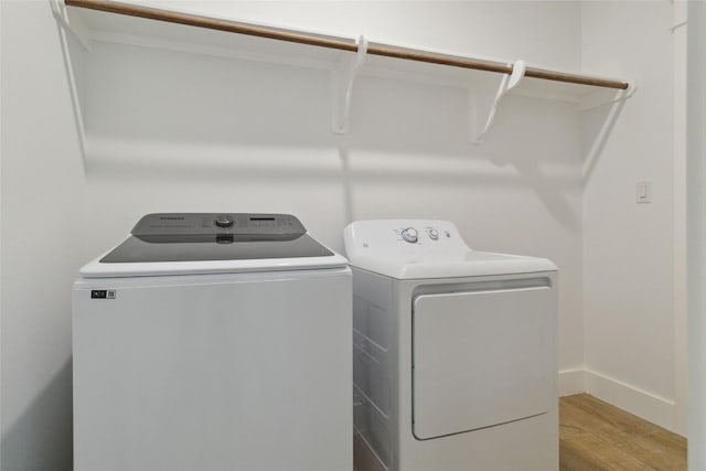 clothes washing area with washer and clothes dryer, laundry area, baseboards, and light wood finished floors