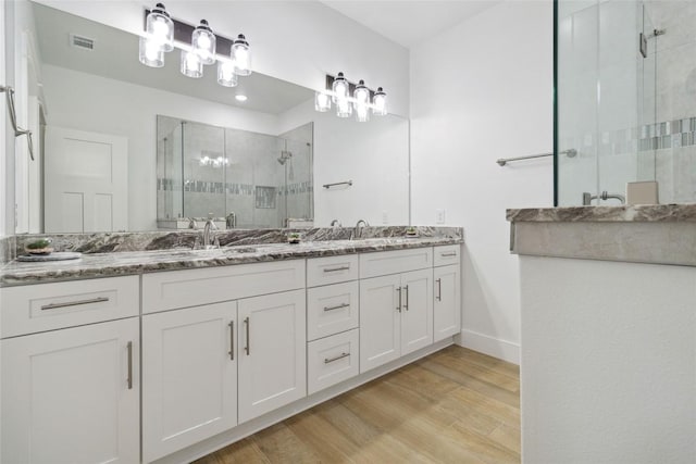 full bath featuring double vanity, wood finished floors, a stall shower, visible vents, and baseboards