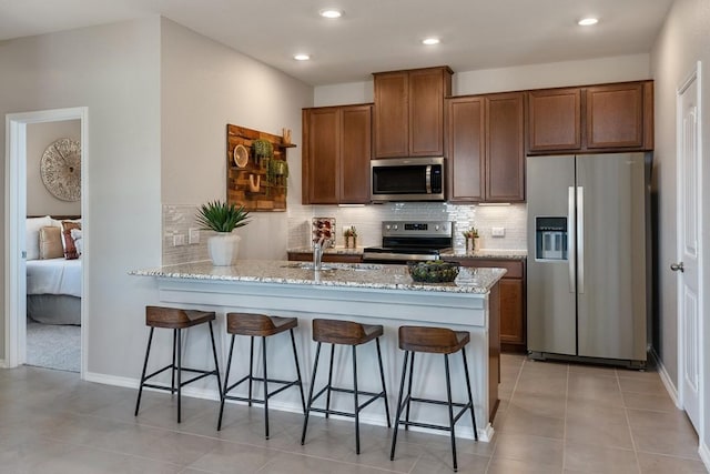 kitchen with light stone countertops, tasteful backsplash, a kitchen breakfast bar, and appliances with stainless steel finishes