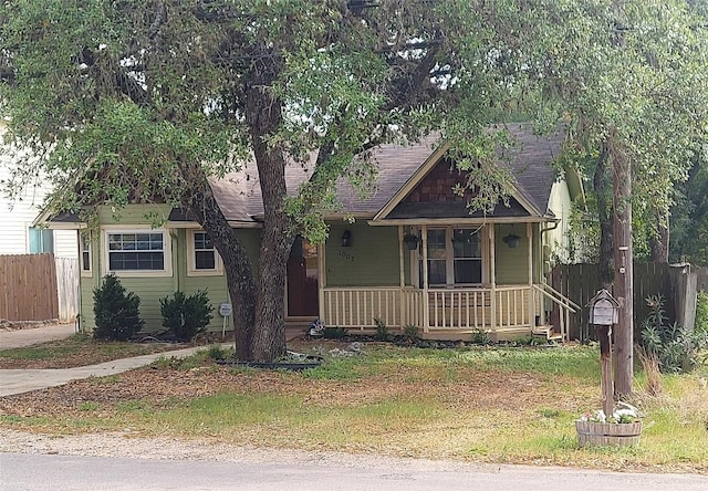 view of front of home with a porch, fence, and a shingled roof
