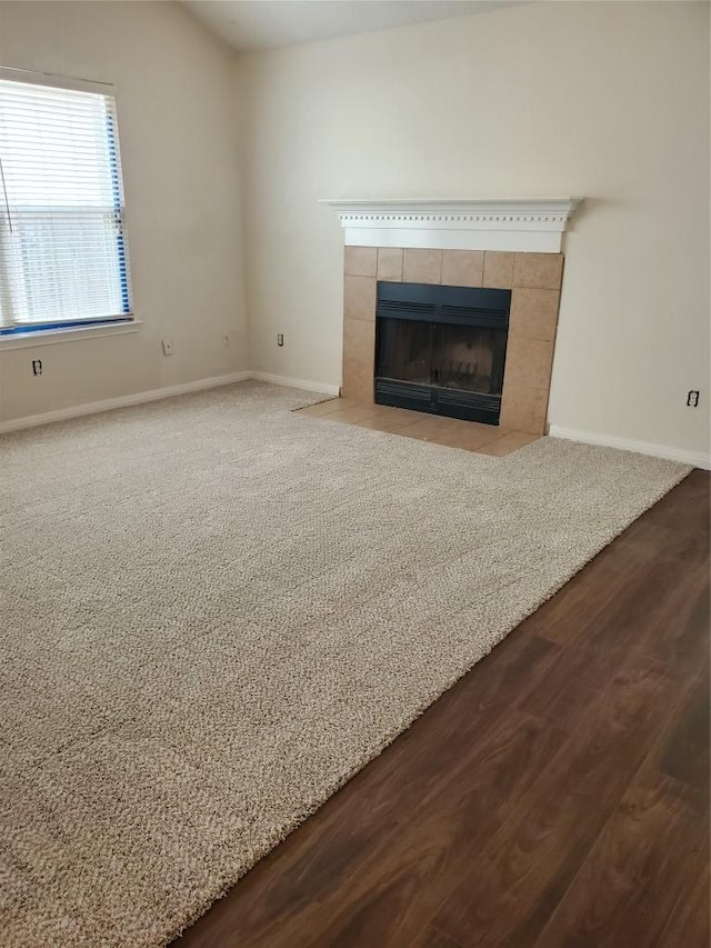 unfurnished living room featuring baseboards, a tile fireplace, and dark wood-type flooring