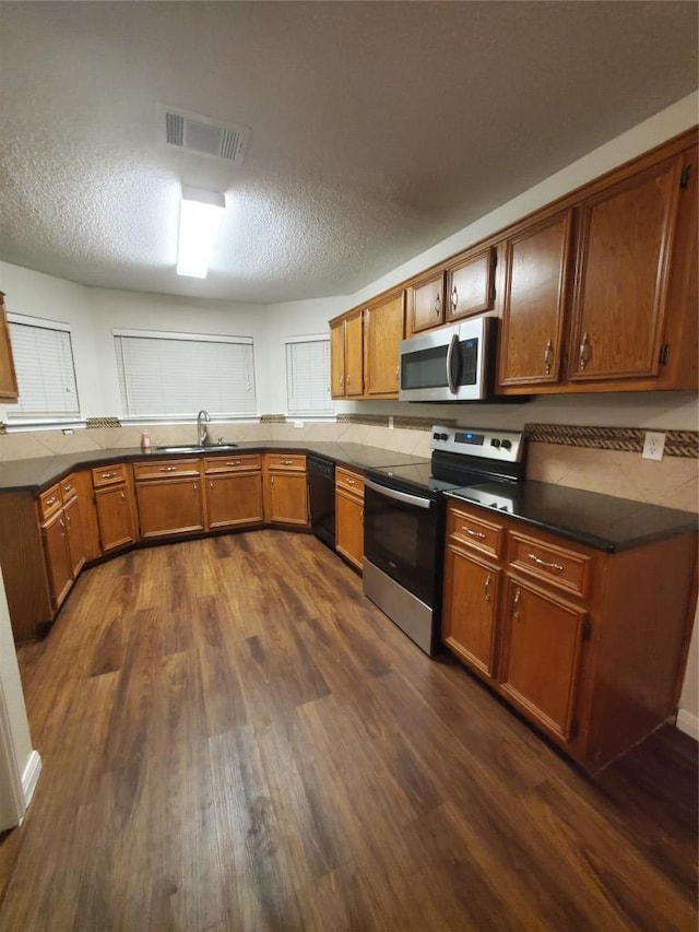 kitchen with a sink, brown cabinetry, visible vents, dark wood-type flooring, and appliances with stainless steel finishes
