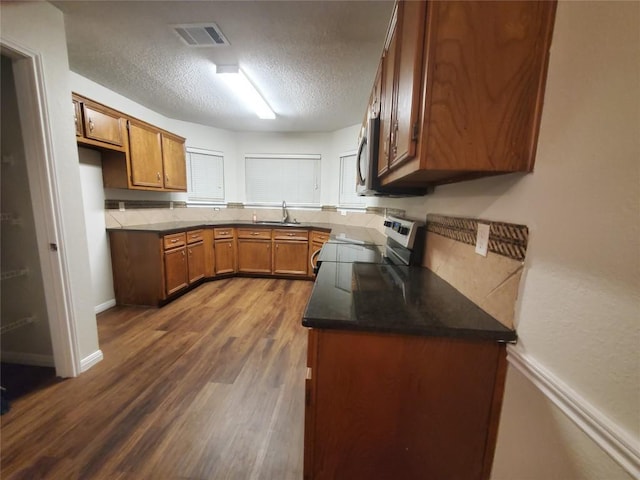 kitchen with brown cabinetry, visible vents, a sink, dark countertops, and stainless steel appliances