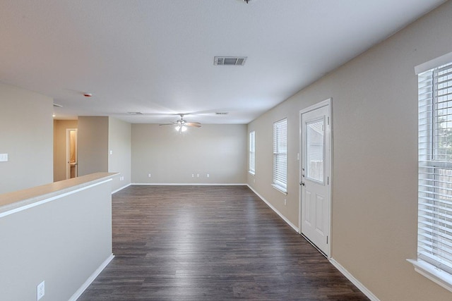 empty room with baseboards, a ceiling fan, visible vents, and dark wood finished floors