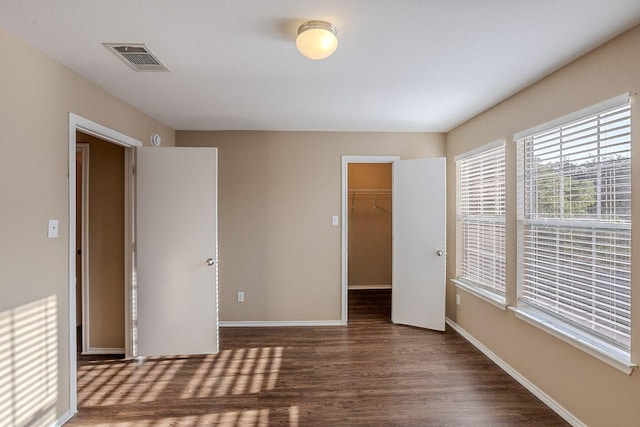 unfurnished bedroom with a closet, wood finished floors, visible vents, a spacious closet, and baseboards