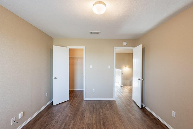 unfurnished bedroom featuring baseboards, a spacious closet, visible vents, and dark wood-type flooring