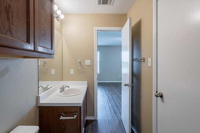 bathroom featuring toilet, baseboards, visible vents, vanity, and wood finished floors