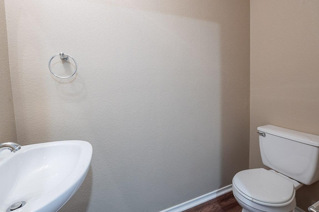 half bath with toilet, wood finished floors, baseboards, and a sink