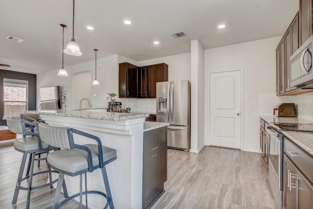 kitchen with a breakfast bar, light wood finished floors, visible vents, a kitchen island with sink, and appliances with stainless steel finishes