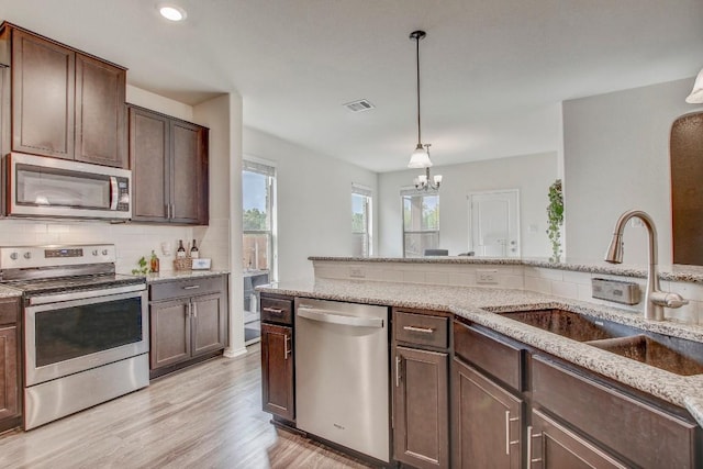 kitchen featuring a sink, stainless steel appliances, visible vents, light wood-style floors, and decorative backsplash