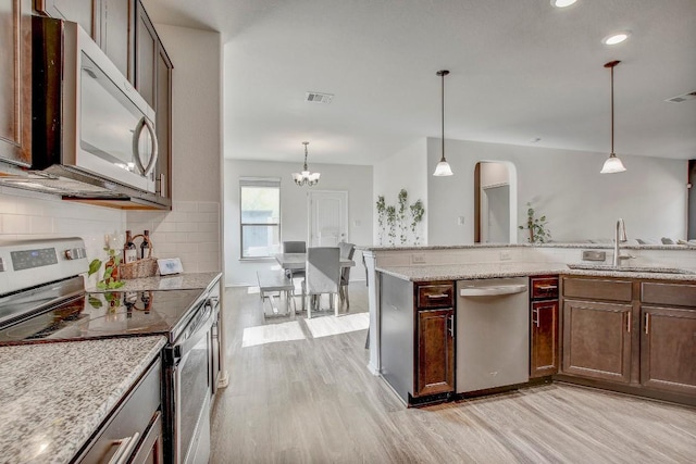 kitchen featuring light wood-style flooring, pendant lighting, a sink, backsplash, and stainless steel appliances