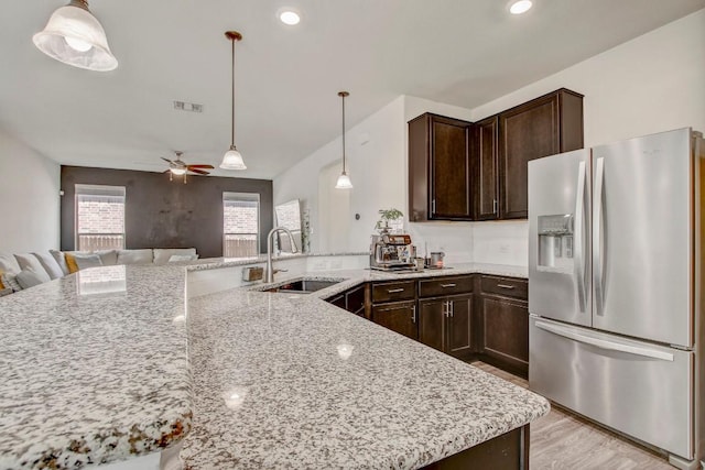 kitchen with stainless steel fridge with ice dispenser, dark brown cabinets, light stone counters, and a sink