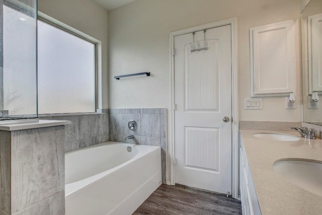full bathroom featuring a garden tub, double vanity, a sink, and wood finished floors