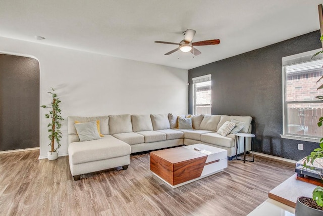 living area featuring a ceiling fan, wood finished floors, baseboards, and arched walkways