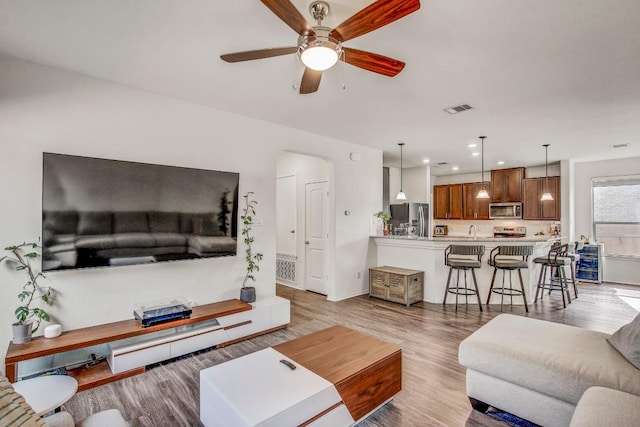 living area with light wood-type flooring, visible vents, recessed lighting, ceiling fan, and arched walkways