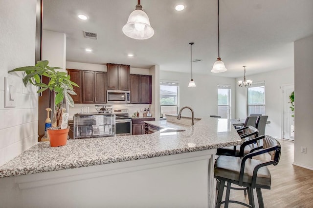 kitchen with a sink, a breakfast bar, visible vents, light wood-style flooring, and appliances with stainless steel finishes